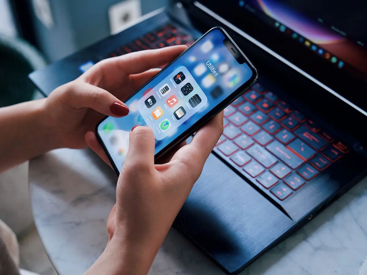 Hands holding a smartphone above a laptop