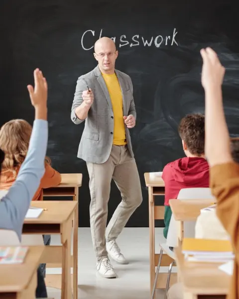 Teacher leading a class while students raise their hands